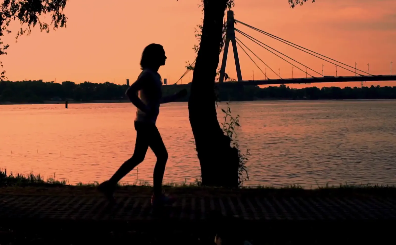 A runner on a riverside path at sunset
